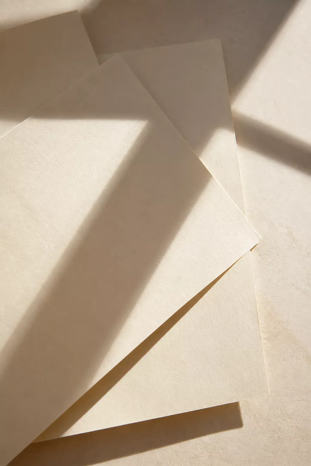 Papeles claros superpuestos con sombras geométricas y luz editorial cálida